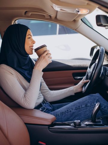 Young modern muslim woman drinking coffee in car